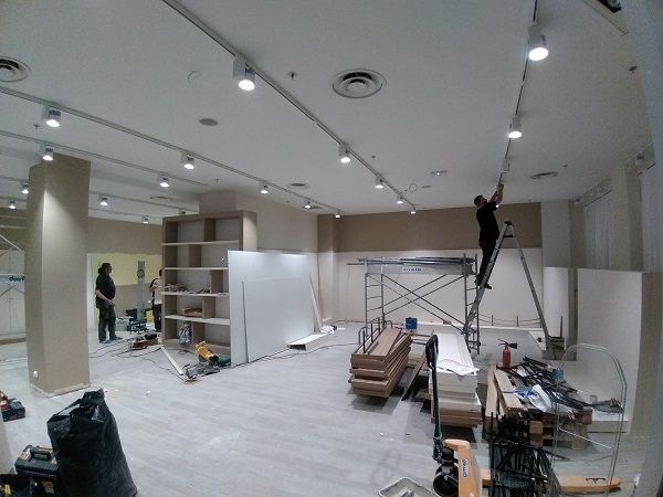 Électricien sur un escabeau posant l'éclairage sur rail d'une boutique en travaux